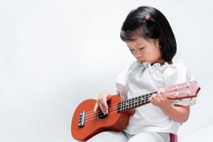 linda garota asiática tocando cavaquinho. fundo branco interno. foto