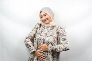 bela jovem asiática muçulmana sorrindo alegremente, com as mãos segurando a barriga, barriga cheia, isolada no fundo branco foto