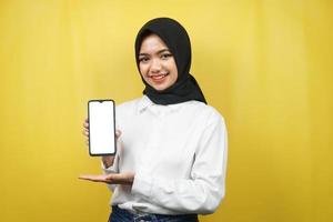 bela jovem muçulmana asiática sorrindo com confiança e entusiasmo com as mãos segurando um smartphone, promovendo um aplicativo, promovendo algo, isolado em um fundo amarelo, conceito de publicidade foto