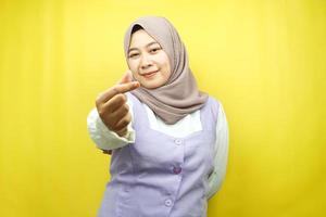 bela jovem muçulmana asiática sorrindo, com sinal de amor coreano, mão perto da câmera, isolado no fundo amarelo foto