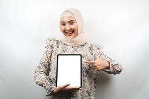 bela jovem muçulmana asiática sorrindo, animada e alegre segurando o tablet com uma tela branca ou em branco, promovendo o aplicativo, promovendo o produto, apresentando algo, isolado no fundo branco