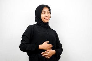 bela jovem asiática muçulmana sorrindo alegremente, com as mãos segurando a barriga, barriga cheia, isolada no fundo branco foto