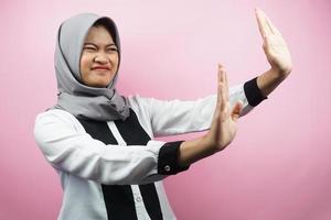 linda jovem muçulmana asiática com a mão rejeitando algo, a mão parando algo, não gostando de algo no espaço vazio, isolado no fundo rosa