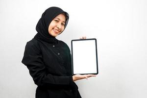 bela jovem muçulmana asiática sorrindo, com a mão segurando um tablet com uma tela branca ou em branco, promovendo o aplicativo, promovendo o produto, apresentando algo, animado e alegre, isolado no fundo branco
