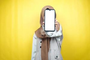mulher muçulmana com as mãos segurando um smartphone, promovendo um aplicativo, promovendo algo, isolado em um fundo amarelo, conceito de publicidade foto