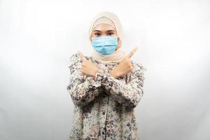 mulher muçulmana usando máscara médica, mão apontando para o espaço vazio, mão apontando para cima apresentando algo, isolado no fundo branco foto