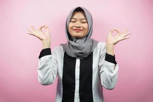 bela jovem muçulmana com as mãos meditando sinais, sorrindo confortável e feliz, isolada no fundo rosa