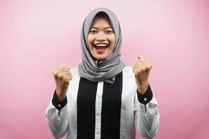 bela jovem asiática muçulmana sorrindo confiante, entusiasmada e alegre com as mãos cerradas, sinal de sucesso, socos, lutando, sem medo, isolado no fundo rosa