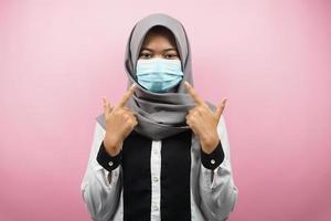 mulher muçulmana usando máscara médica com a mão apontando para a máscara, movimento antivírus corona, movimento anti covid-19, movimento de saúde usando máscara, isolado no fundo rosa foto