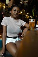 jovem negra com penteado afro olhando para a câmera, sentado em um bar
