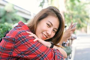 jovens mulheres asiáticas sentam e sorriem ao longo da rua, apreciando seu estilo de vida de cidade em uma manhã de um fim de semana, esperando por atividades ao ar livre. jovem e seu estilo de vida na cidade. estilo de vida e conceito ao ar livre foto