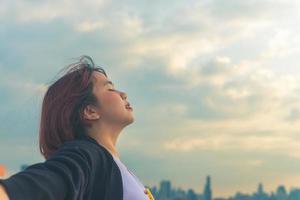 Mulher asiática sozinha sentada no telhado de um prédio ver a vista da cidade no pôr do sol da noite. foto