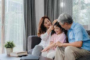 avós asiáticos beijam a bochecha da neta em casa. sênior chinês, velha geração, avô e avó usando o tempo para a família relaxam com uma criança jovem deitada no sofá no conceito de sala de estar. foto