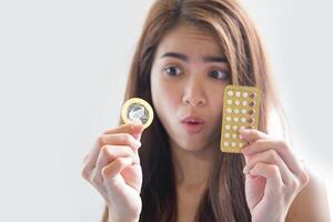 jovem segurando uma camisinha e pílulas anticoncepcionais evita a gravidez foto