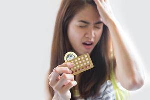 jovem segurando uma camisinha e pílulas anticoncepcionais evita a gravidez foto
