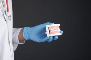 mão do médico segurando um modelo de dente dentário de plástico na mesa foto