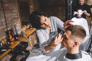 uma cabeleireira raspa a cabeça de uma cliente com um aparador elétrico em uma barbearia
