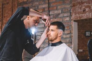 jovem barbeiro rapa a cabeça do cliente com um aparador elétrico foto