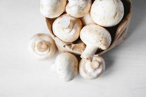 cogumelos champignon em saco de papel sobre uma mesa de madeira branca foto