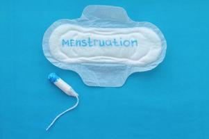 almofada feminina com a inscrição menstruação e um tampão em um fundo azul. o conceito de ciclo menstrual. foto