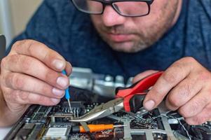 um homem conserta um computador, solda uma placa, conserta eletrônicos e tecnologias modernas foto