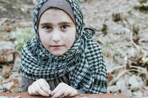 uma criança refugiada na guerra, uma garota muçulmana com o rosto sujo nas ruínas, o conceito de paz e guerra, a criança está chorando e esperando por ajuda. foto