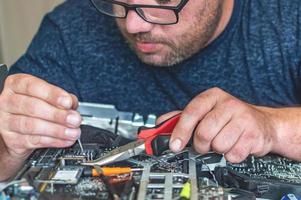 um homem conserta um computador, solda uma placa, conserta eletrônicos e tecnologias modernas foto