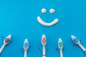 escovas de dentes coloridas em forma de personagens de desenhos animados sobre um fundo azul com um sorriso desenhado com pasta de dente. a visão de cima. o conceito de higiene familiar. foto
