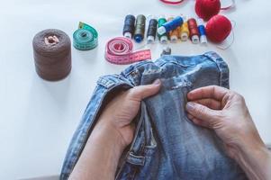 mãos de mulheres, um alfaiate costura roupas em uma mesa sobre a qual repousam carretéis de linha foto