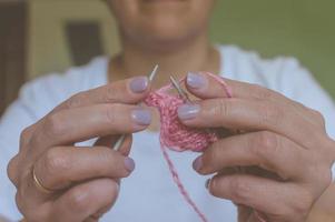 garota tricô fios com agulhas de tricô e crochê em casa. em uma camiseta branca. malhas de mão foto