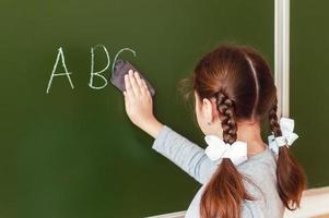 menina adolescente com cabelo ruivo lava o quadro na aula durante a aula foto