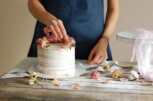 as mãos das mulheres decoram o bolo de creme com flores frescas. foto horizontal.