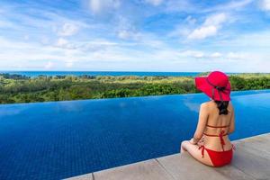 jovem asiática de biquíni com chapéu sentada à beira da piscina na praia, férias de verão, phuket, tailândia foto