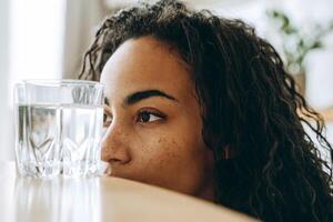 jovem negra olhando para um copo de água enquanto está sentada na cozinha foto