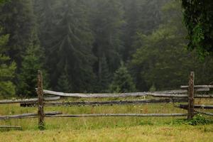 Prado de outono com uma cerca de madeira velha em uma fazenda perto, nas montanhas esfumaçadas em um dia de nevoeiro. destino de viagem cênica, montanhas dos Cárpatos foto