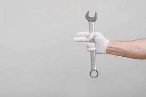 um trabalhador, construtor, reparador, faz-tudo, mãos com luva de proteção segurando a chave inglesa em fundo branco. mock up cópia espaço.