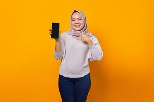 mulher asiática jovem e alegre mostrando a tela em branco do smartphone isolada sobre fundo amarelo