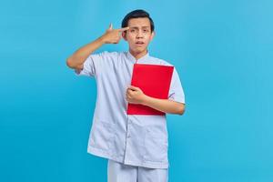 jovem enfermeiro bravo segurando uma pasta vermelha e apontando o dedo para a cabeça sobre fundo azul