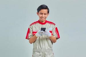 Homem bonito sorridente usando uniforme mecânico usando telefone celular isolado em um fundo cinza foto