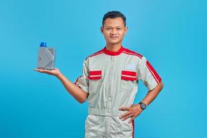 retrato de um jovem mecânico asiático sorrindo, mostrando a garrafa de plástico de óleo de motor na palma da mão sobre fundo azul