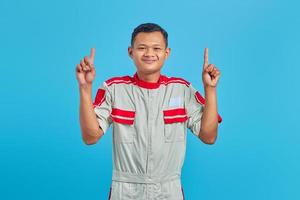 retrato de um jovem mecânico asiático sorridente enquanto levanta o dedo isolado sobre fundo azul foto