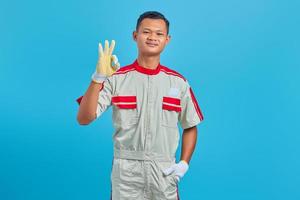 retrato de um jovem mecânico asiático sorridente, fazendo um gesto de aprovação, mostrando o símbolo de aprovação isolado sobre fundo azul. foto