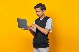 retrato de jovem bonito usando laptop, olhando sério, fazendo trabalhos de escritório em fundo amarelo foto