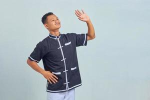retrato de jovem asiático sorrindo, vestindo quimono taekwondo, fazendo um gesto com as palmas das mãos isoladas em um fundo cinza