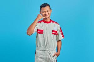 retrato de um jovem mecânico asiático sorridente, fazendo um sinal de chamada sobre fundo azul. foto