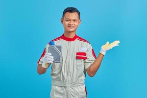retrato de um jovem mecânico asiático sorridente, mostrando a garrafa de plástico de óleo de máquina e apontando para copiar o espaço com a palma da mão sobre o fundo azul