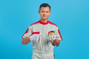 retrato de um jovem mecânico asiático sorridente, carregando uma xícara de café na mão sobre um fundo azul.