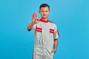 retrato de um jovem mecânico asiático fazendo stop motion com a palma da mão isolada sobre fundo azul. foto
