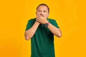 surpresa jovem asiática cobrindo a boca com a mão em fundo amarelo foto