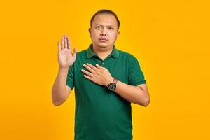 retrato de bonito homem asiático xingando com as mãos no peito e as palmas das mãos abertas sobre fundo amarelo foto